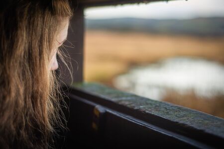 Background Image With Copy Space of a Young Femal Bird Watcher Looking Out from a Hide