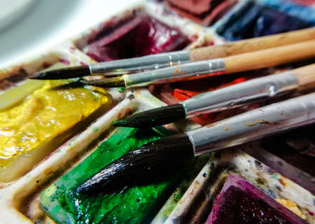 four brushes on a background of multi-colored watercolor paint taken in macro shootingの写真素材