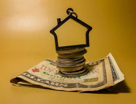 a symbol in the form of a house on the background of American dollar bills and a stack of iron coins, like the sale of housesの写真素材
