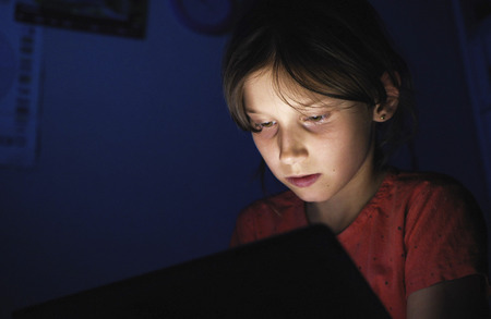 Dolly shot caucasian girl lying in bed playing tablet in social internet in dark blue light under...