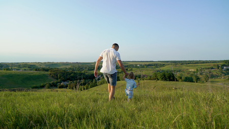 Father and daughter share love walking together in high grass field. Young caucasian happy father have leisure time with toddler daughterの写真素材
