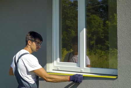 Man worker in safety glasses cleaning surface for metal sill installation. Builder preparing workplace for assembling PVC window construction outside building. Technology, exterior design conceptの写真素材