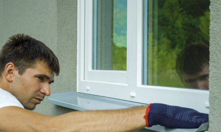Man worker in protective gloves measuring external frame and PVC window metal sill size. Builder...