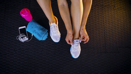 Top view of a fit woman seated on the floor of a gym tying shoelaces sneakers. Healthy lifestyle. Sport and cardio workout conceptの写真素材