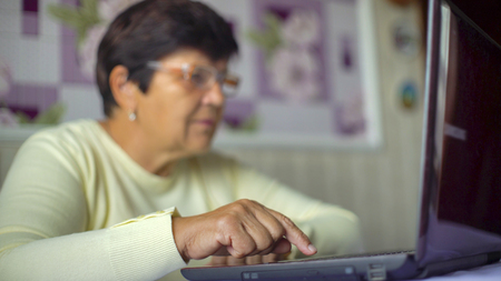 Senior old woman in eyeglasses surfing internet on laptop at home with free space and copy space. White caucasian female pensioner using computer shopping online. Technology, communication conceptの写真素材
