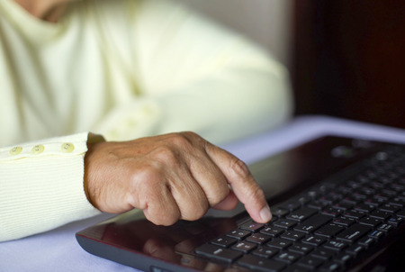 Closeup senior old woman hand on laptop keyboard surfing and browsing internet at home with free and copy space. Technology, communication, information conceptの写真素材