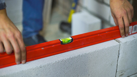 closeup of builder checking evenness of aerated concrete wall with bubble level