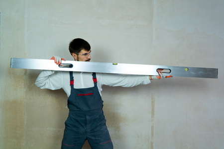 builder holds construction ruler with empty wall on background