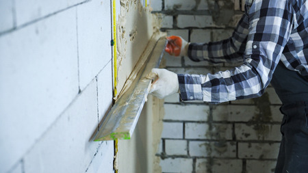 view of builder hands in gloves using construction ruler for plastering