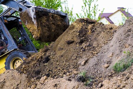 partial view of excavator bucket unloading soil
