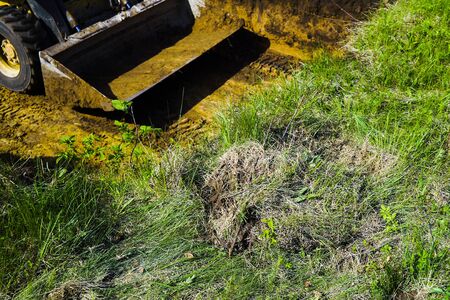 cropped view of bulldozer bucket at excavation works on grassy sector