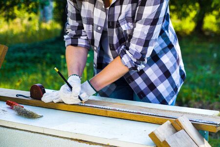 cropped shot of handywoman measures wooden plank and puts mark on it with pencil