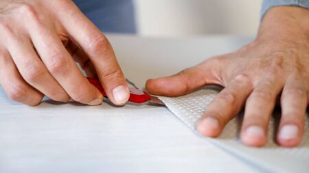 closeup male hands preparing new bended wallpaper roll with stationery knife on table indoor