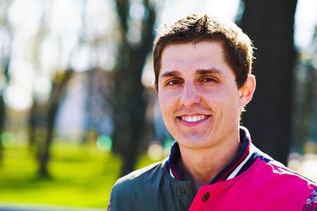 Cheerful young man talking to camera in sunny park