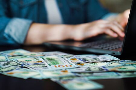 Entrepreneur working online on laptop and receiving income in dollar billsの写真素材