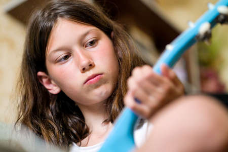 Portrait of little girl playing blue ukulele guitar at home