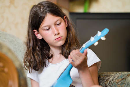 Little girl playing ukulele guitar at home