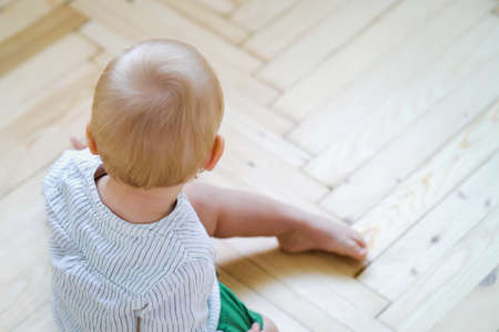 Little blonde boy sitting on wooden floor indoorsの写真素材