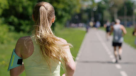 Blonde woman with ponytail wearing smartphone attached to shoulder running raceの写真素材