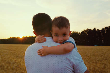 Father holding little son in arms and walking towards sunsetの写真素材