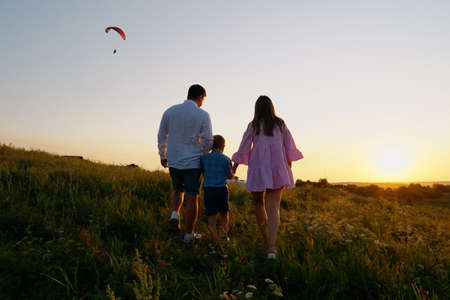 Family holding hands and walking in meadow at sunsetの写真素材