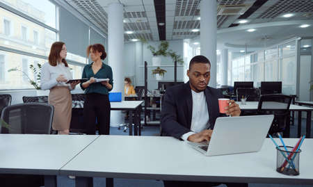 African American businessman with coffee using laptop in open space officeの写真素材
