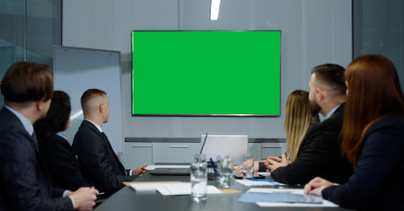 Green screen on wall in office during online meeting, executives sitting at table and looking at...