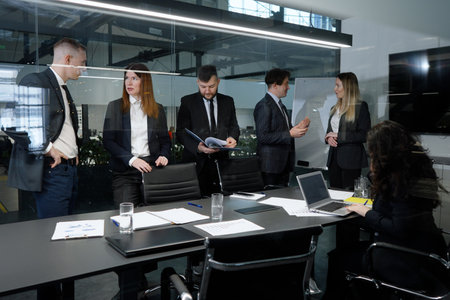 Business people working in office, some discussing projects, one man looking at papers, one woman working on laptop, viewed from behind glass wall. concept of businessの写真素材