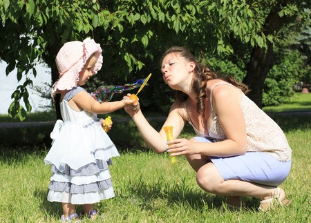 Beautiful mother and daughter blow bubbles in a city park.の写真素材
