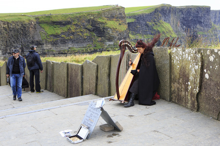 Clare, Ireland - August 25, 2014: Woman playing the harp for tourists. Cliffs of Moher the most...