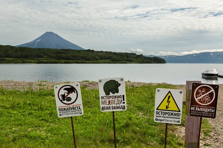 Kamchatka Peninsula, Russia - August 13, 2016: Signs warn of the danger of meeting tourists with bears in the background of Kurile Lake and Ilyinsky volcano. South Kamchatka Nature Park.のeditorial素材