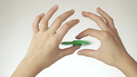 Hands of a teenage girl spin a green fidget spinner on a white backgroundの写真素材