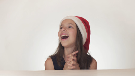 Beautiful happy girl teenager in a Santa Claus hat look and emotionally expresses a surprise on a...