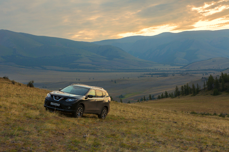 Altai Krai, Russia - July 15, 2015: Crossover Nissan X-TRAIL on the hillside in the Kurai steppe against the backdrop of the North Chuy ridge at dawn.のeditorial素材