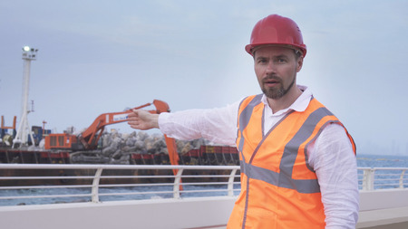 Man in a helmet, architect, engineer, manager tells about the course of repair work of the coastline...