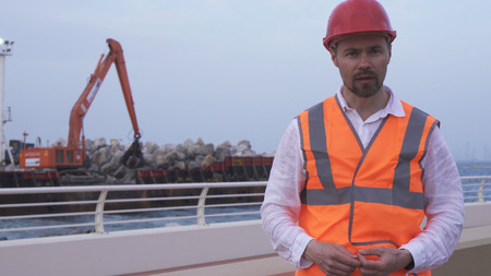 Man in a helmet, architect, engineer, manager tells about the course of repair work of the coastline with a stoneの写真素材