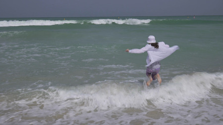 Teenage girl in clothes joyfully jumping in the waves of the Persian Gulf on the beach of Dubaiの写真素材