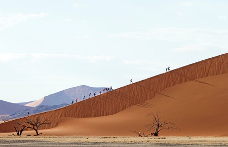 Some tourists climbing a sand dune in the Sossusvlei park, Namibiaの写真素材