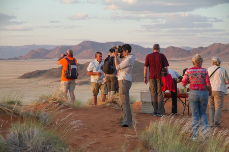 SOSSUSVLEI PARK, NAMIBIA -  MAY 6, 2014: a group of tourists is enjoying the sunset in the namibian landscape, photographing, drinking and enjoying the sunsetのeditorial素材