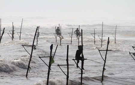 Some fisherman are fishing on a stick in the middle of the sea