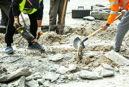 Worker on a road construction sites removing the old asphalt layer using pick hammers. Infrastructure industry.