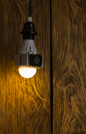 Diy led lamp with huge heatsink with ventillator on it. Ugly and messy fast handmade assembly. High power led with half-spherical diffuser used. Dark wooden background with selective focus.の写真素材