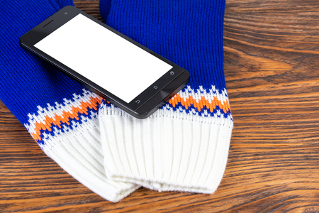 blue and white knited mittens with cellphone on wooden backgroundの写真素材