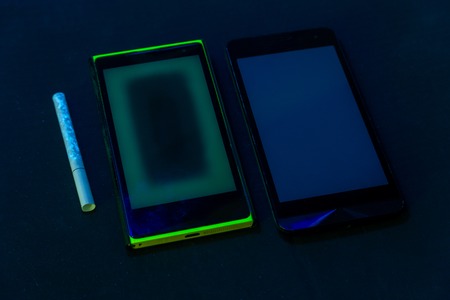 used phones and cigarette under UV light on black bckground with selective focusの写真素材