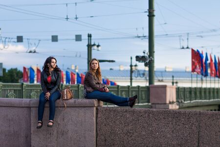 SAINT-PETERSBURG, RUSSIA - JULY 22, 2015: Two pretty young women sitting on granite fence of the bridge.のeditorial素材