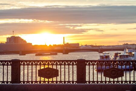 Bridge fence at Saint-Petersburg at summer sunrise and blurred Neva river background with boats and bridge.の写真素材