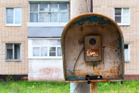 Old public russian wired urban telephone post - useless abandoned and broken. Horizontal shot with selective focus and blurred suburbs condominium house in background.の写真素材