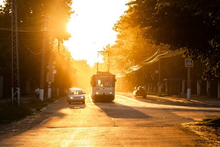 TULA, RUSSIA - JUNE 6, 2013: Car and tram on traffic light stop under golden sun backlight. Air glowing bright.のeditorial素材