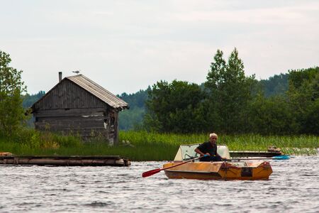 REPUBLIC OF KARELIA, RUSSIA - JULY 2, 2013: Old gray-haired tanned man sailing on boat with paddles...