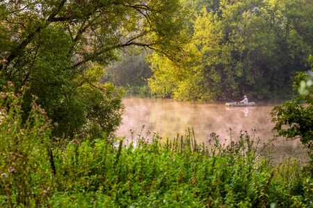 TULA, RUSSIA - AUGUST 12, 2013: A man fishing on river at inflatable boat at foggy summer morning under green foliage.のeditorial素材